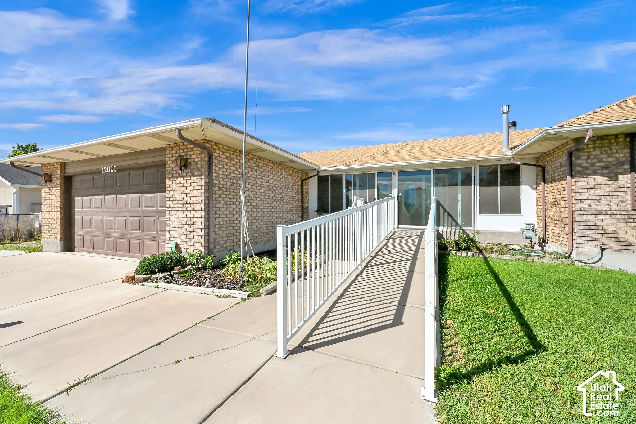 Brick exterior featuring a two-car garage with overhead door, concrete driveway, and a white ramp leading to the entry