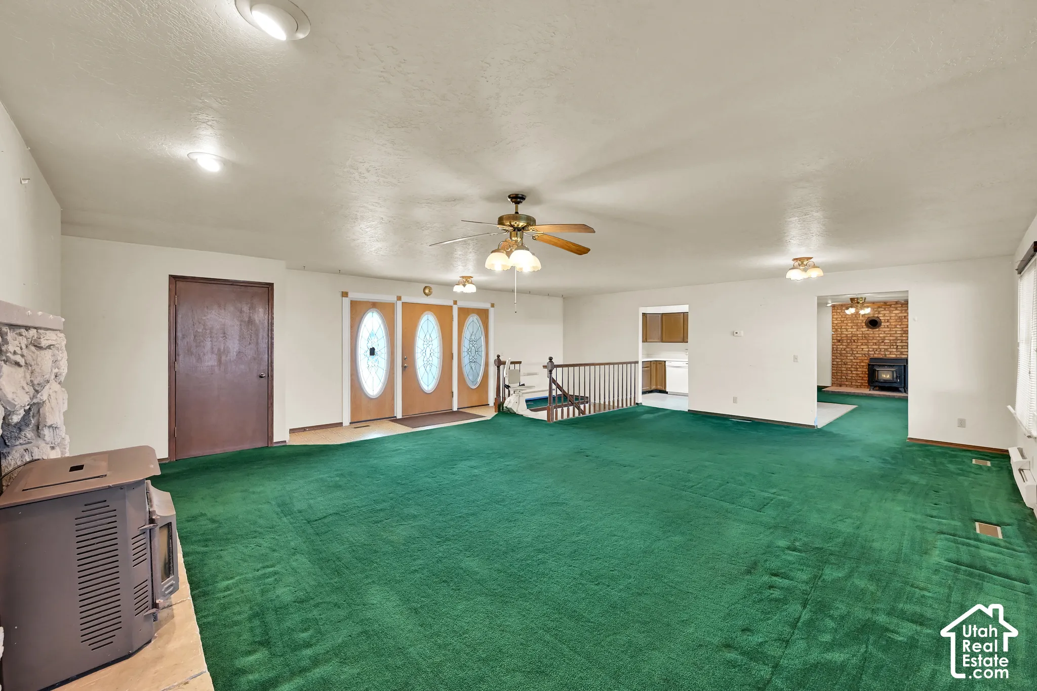 Spacious living area featuring extensive green carpeting, multiple ceiling fans, and recessed lighting