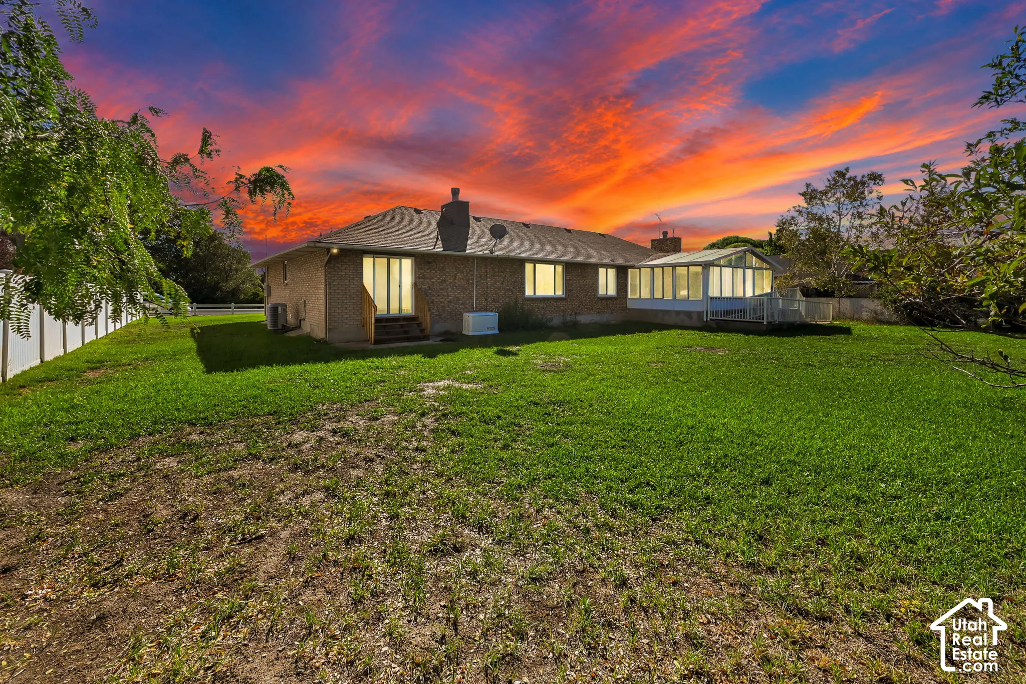 Brick exterior, sunroom with multiple windows, rear exterior steps, white privacy fence, mature trees