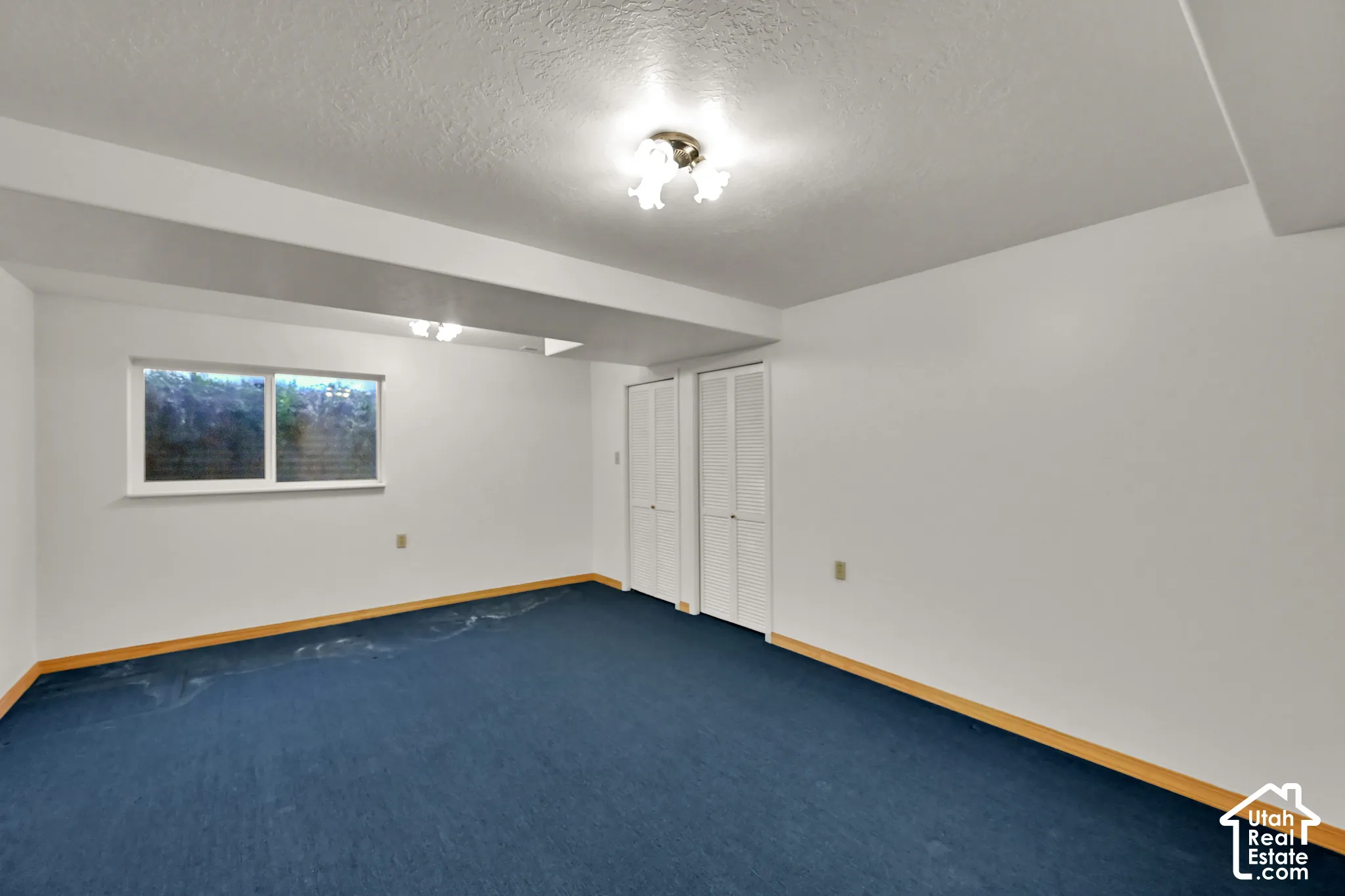 White walls with blue carpeting, a single window, and bi-fold closet doors