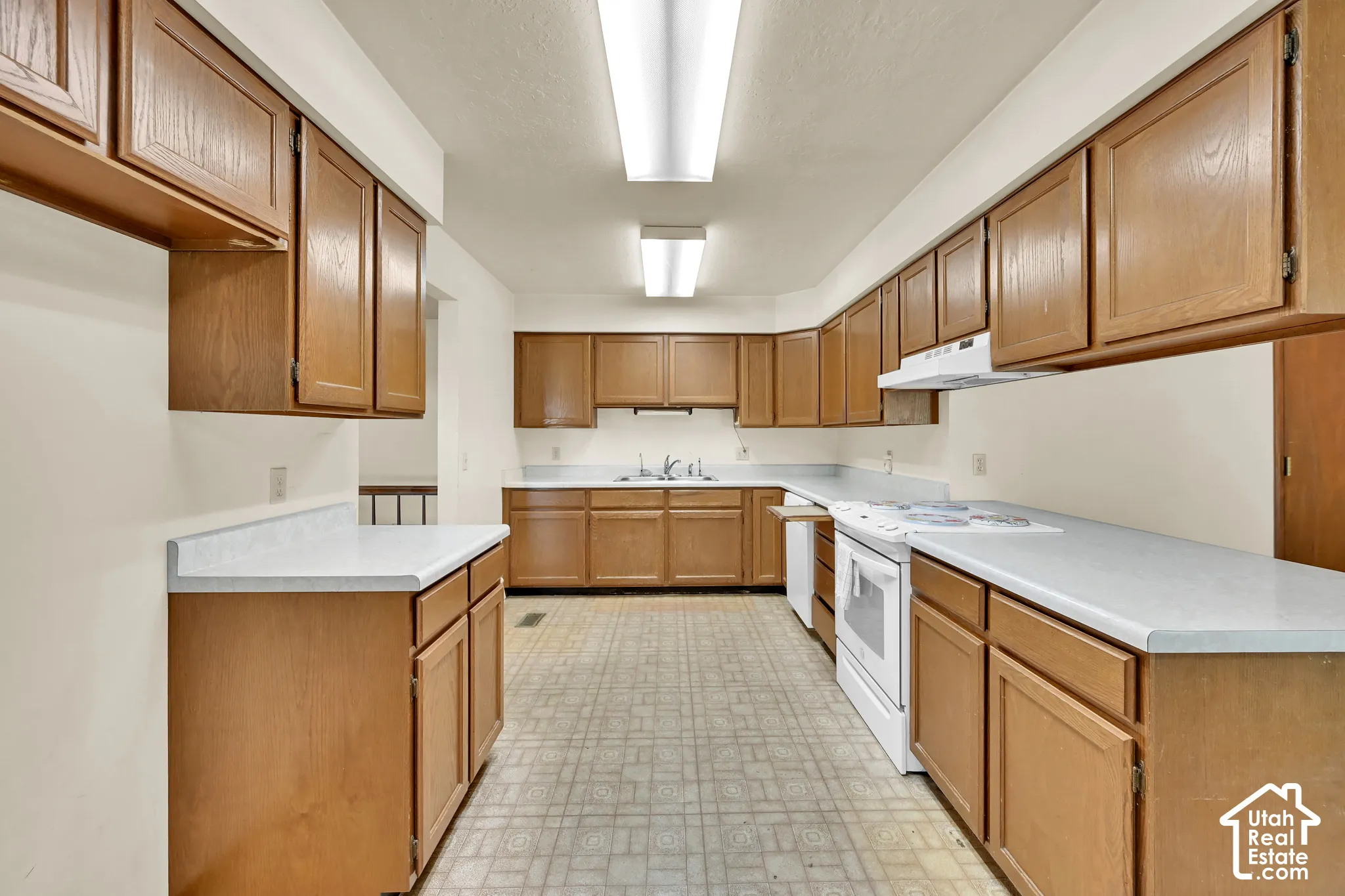 Extensive wood cabinetry, white countertops, built-in cooktop, white range hood, and integrated sink