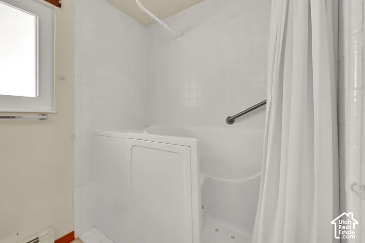 Walk-in tub with a grab bar, white tile surround, and a window providing natural light