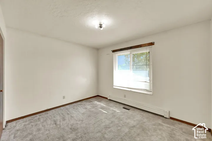 Carpeted flooring, white walls, window with blinds, ceiling-mounted light fixture, and wooden trim