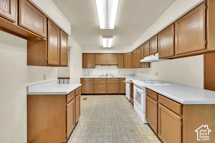 Extensive wood cabinetry, white countertops, built-in cooktop, white range hood, and integrated sink