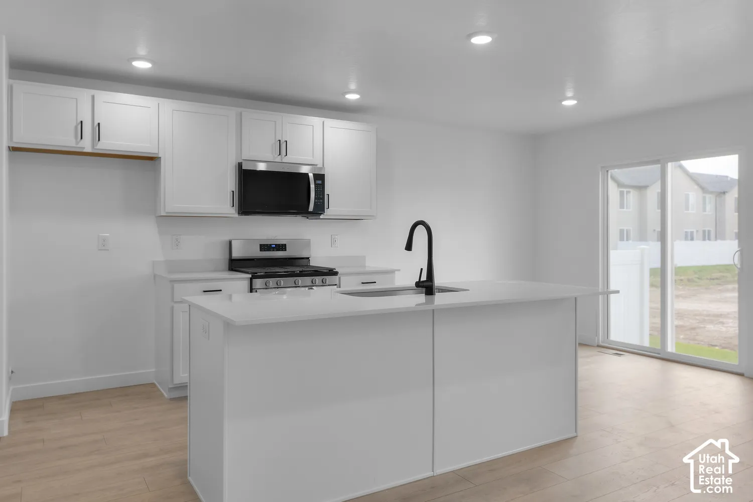 Modern kitchen featuring white cabinetry, stainless steel appliances, a center island with sink, contemporary black faucet, and wood-finish flooring