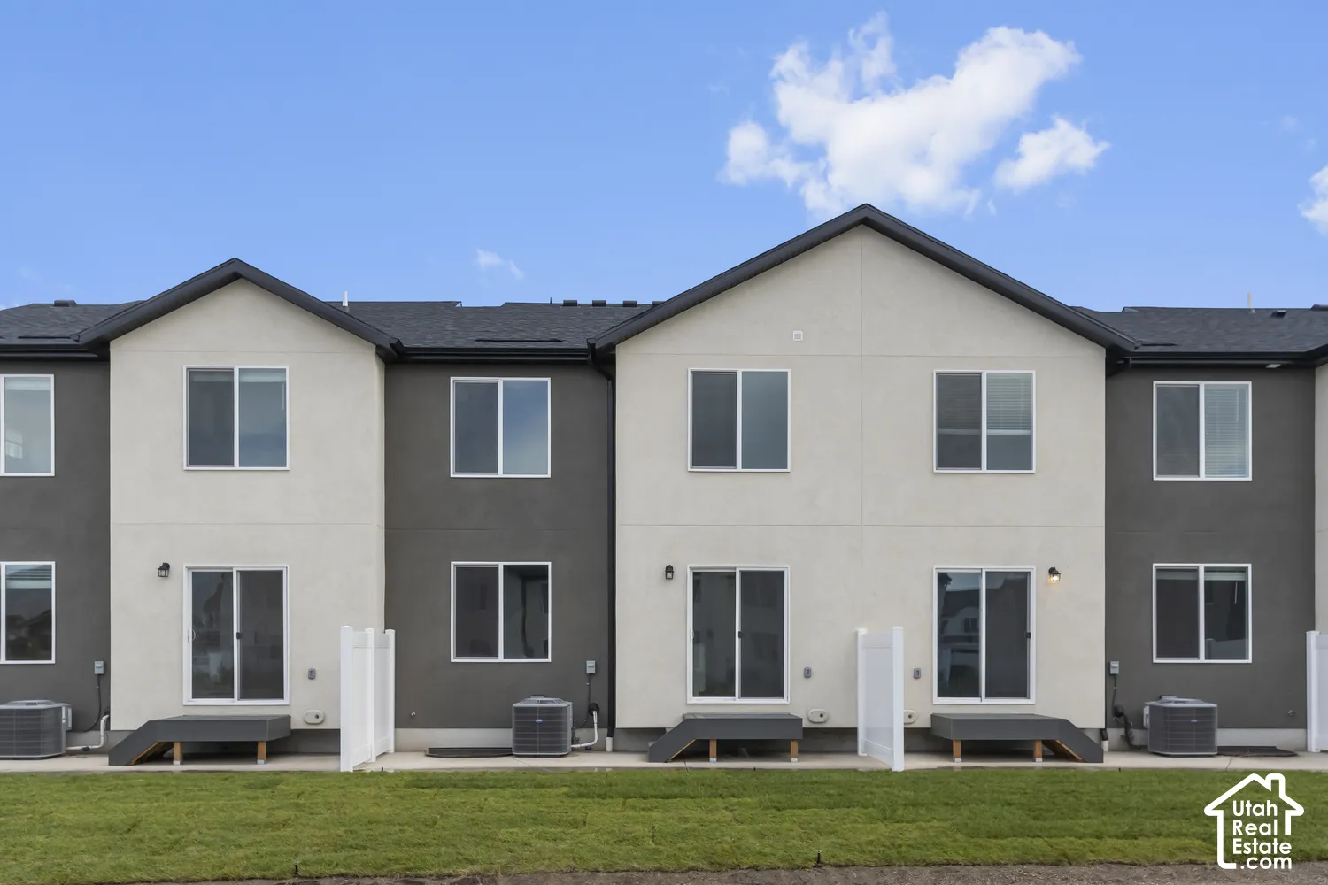 Modern townhome exterior with contrasting stucco finishes, multiple dual-pane windows, and sliding glass doors providing access to the yard