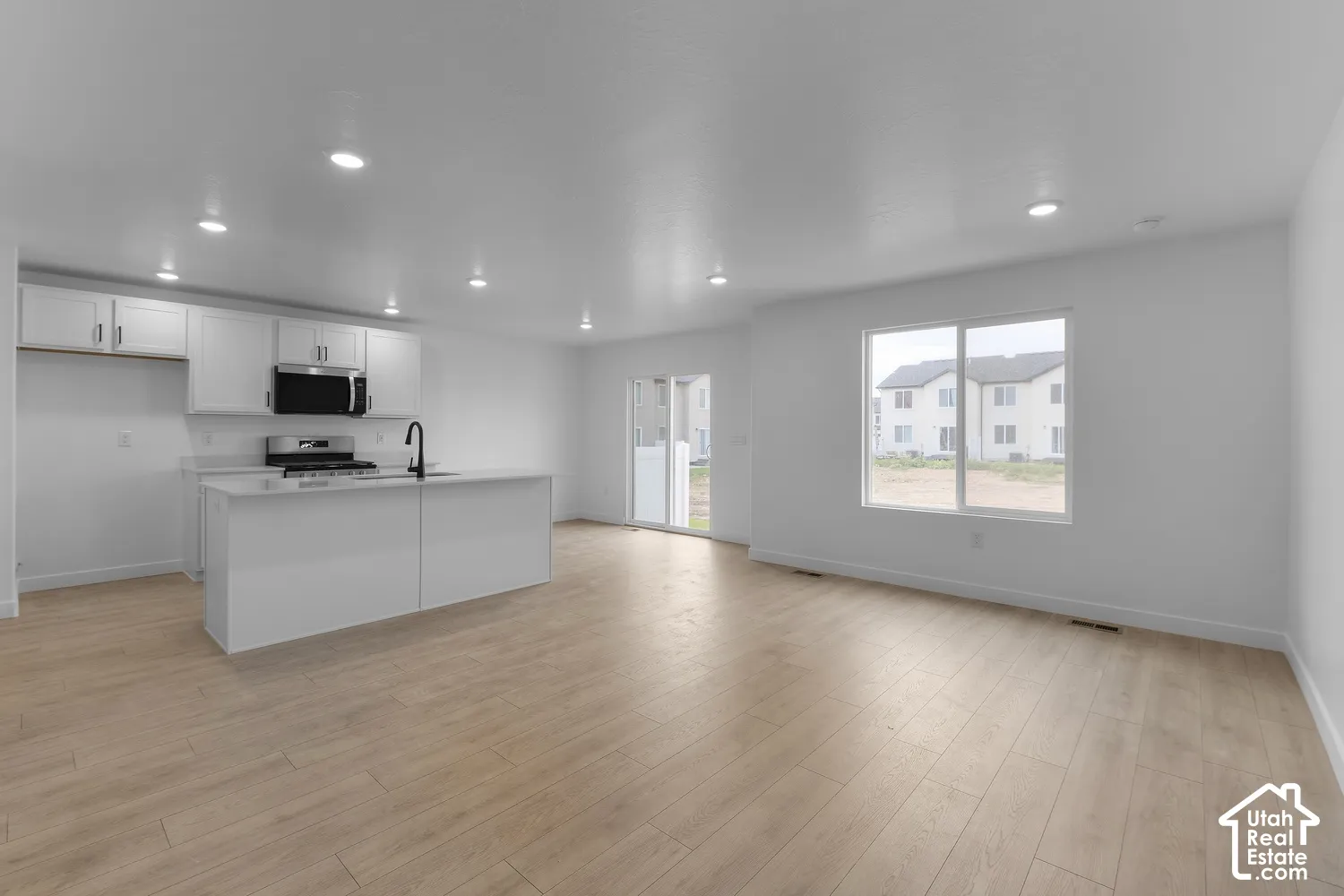 Expansive open-concept living area featuring wood-finish flooring, recessed lighting, and a kitchen with white cabinetry, stainless steel appliances, and an island with a sink