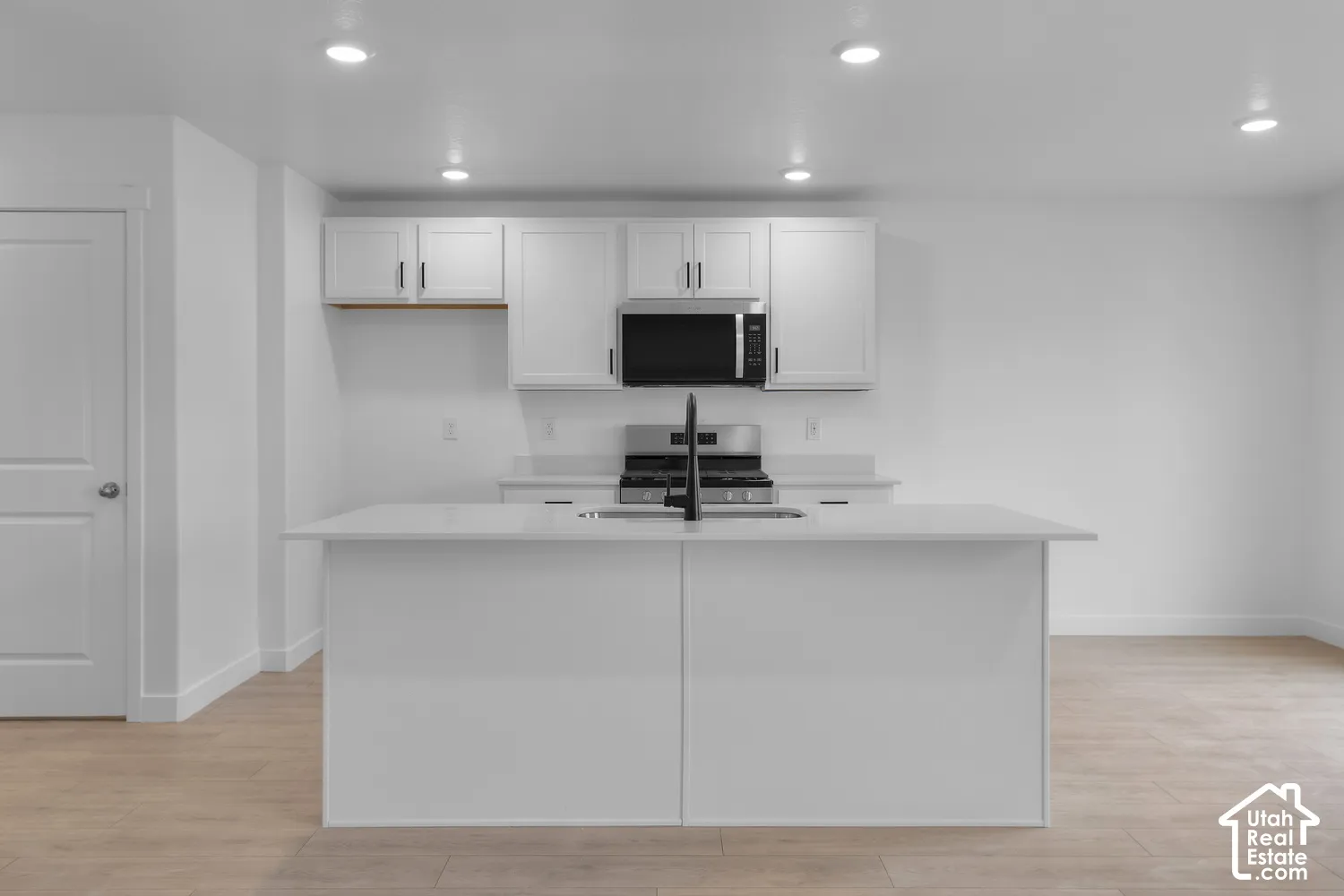 Kitchen featuring white cabinetry, a central island with an integrated sink, stainless steel appliances, recessed lighting, and wood-finish flooring