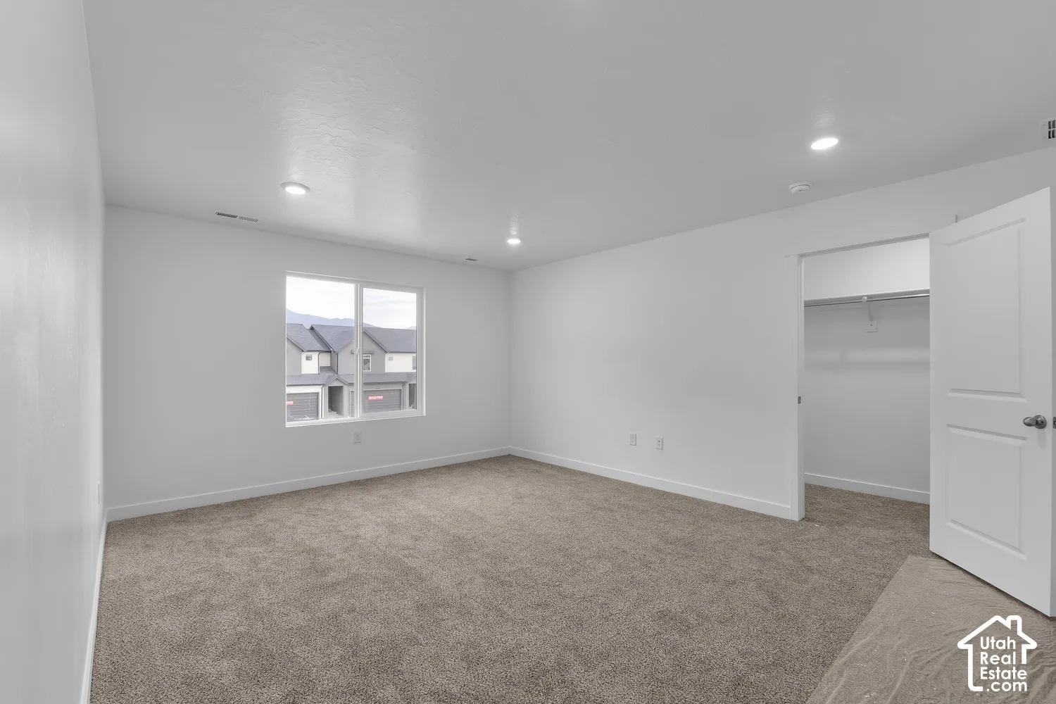 Broadloom carpeting, recessed ceiling lighting, a window with exterior visibility, and an open closet with a hanging rod