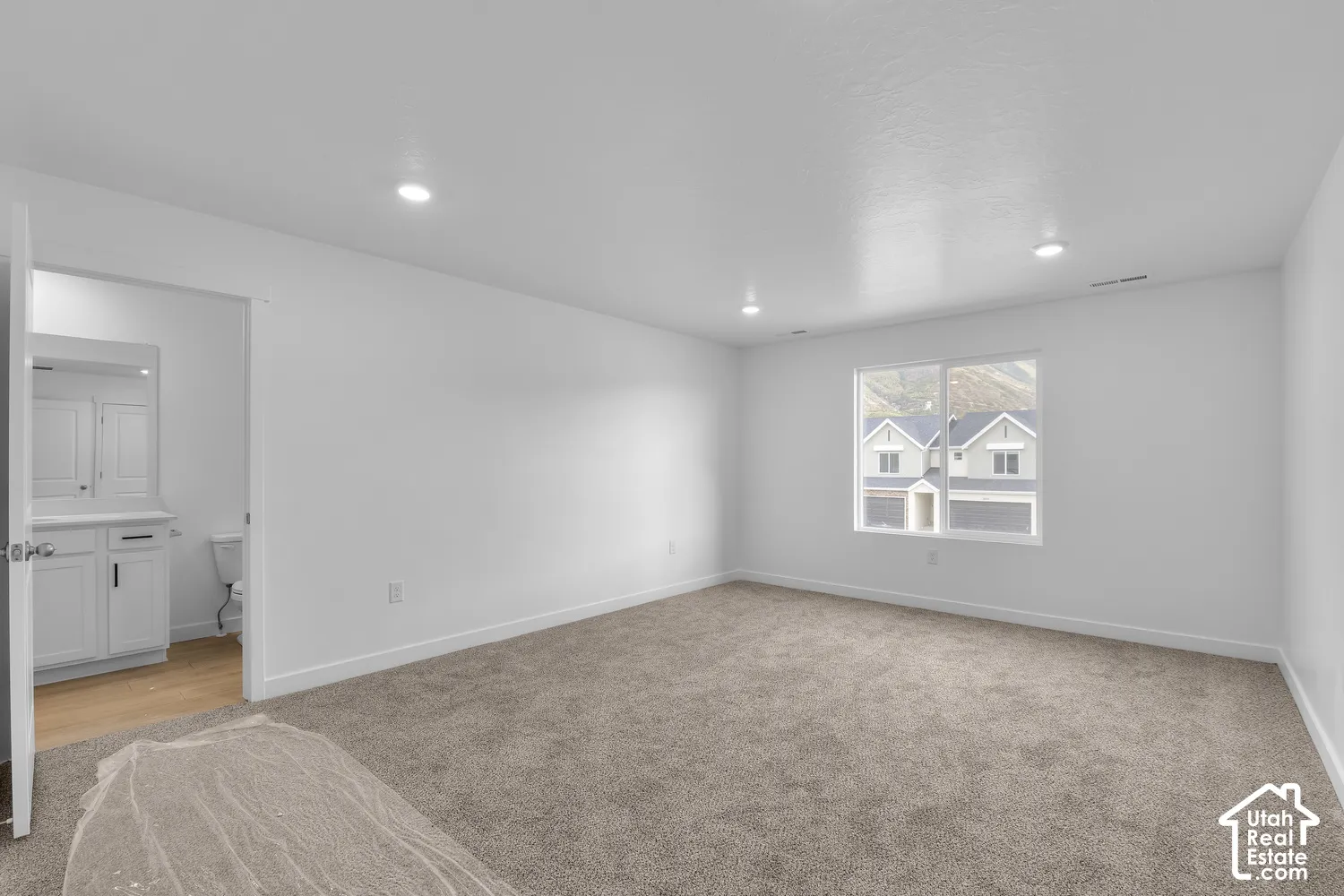 Recessed lighting, carpet flooring, a window offering exterior scenery, and an adjoining room featuring a vanity with a mirror and cabinet storage