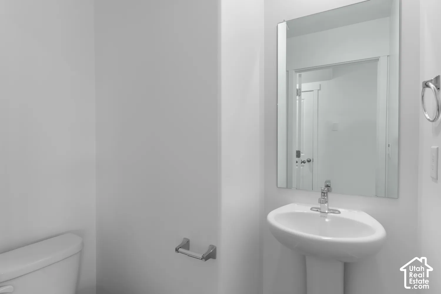 Pedestal sink with chrome faucet, wall-mounted rectangular mirror, and white toilet