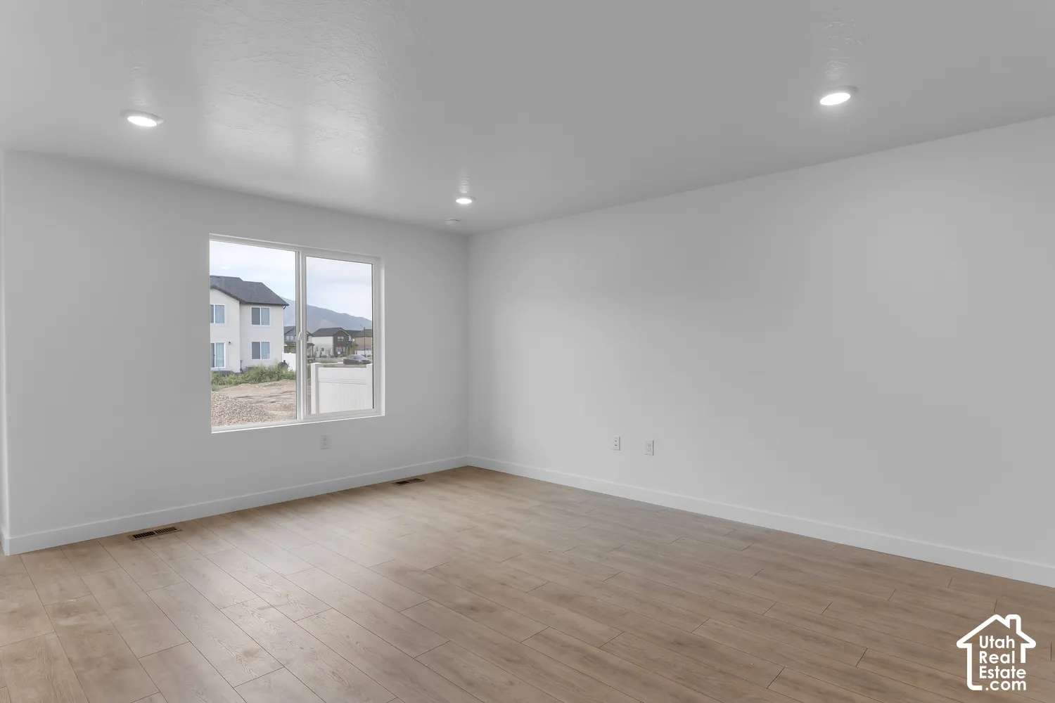Recessed ceiling lighting, wood-finish flooring, white walls, and a large window