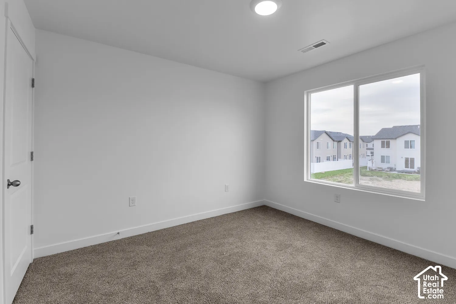 Spacious room featuring neutral carpeting, a large window, white walls, and a ceiling-mounted light fixture
