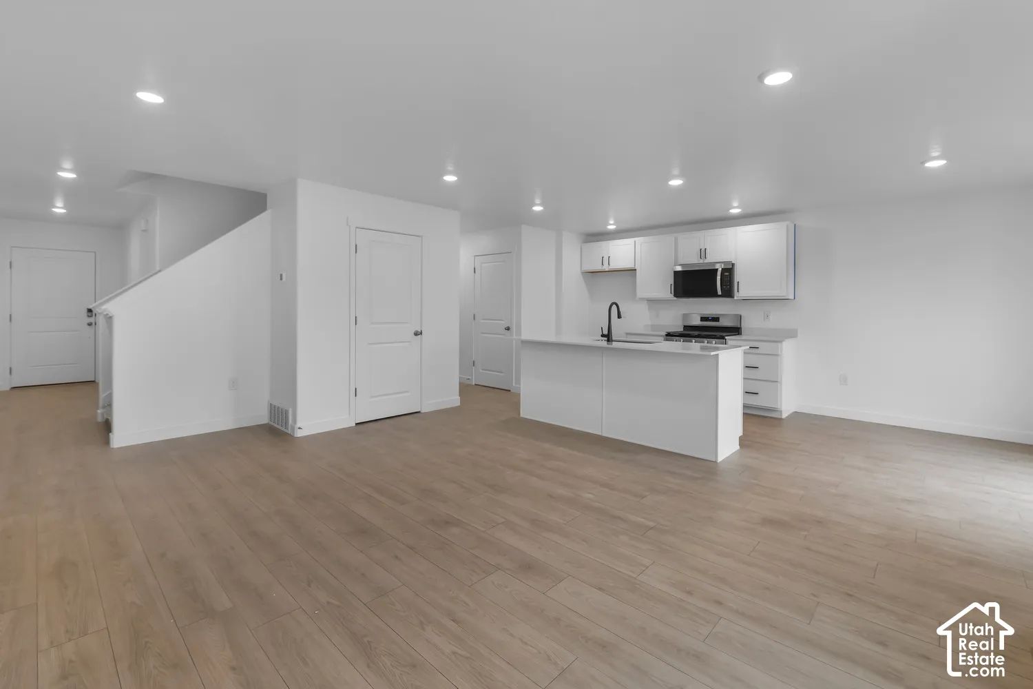 Open-concept living area featuring wood-finish flooring, recessed lighting, and a kitchen with white cabinetry and a central island