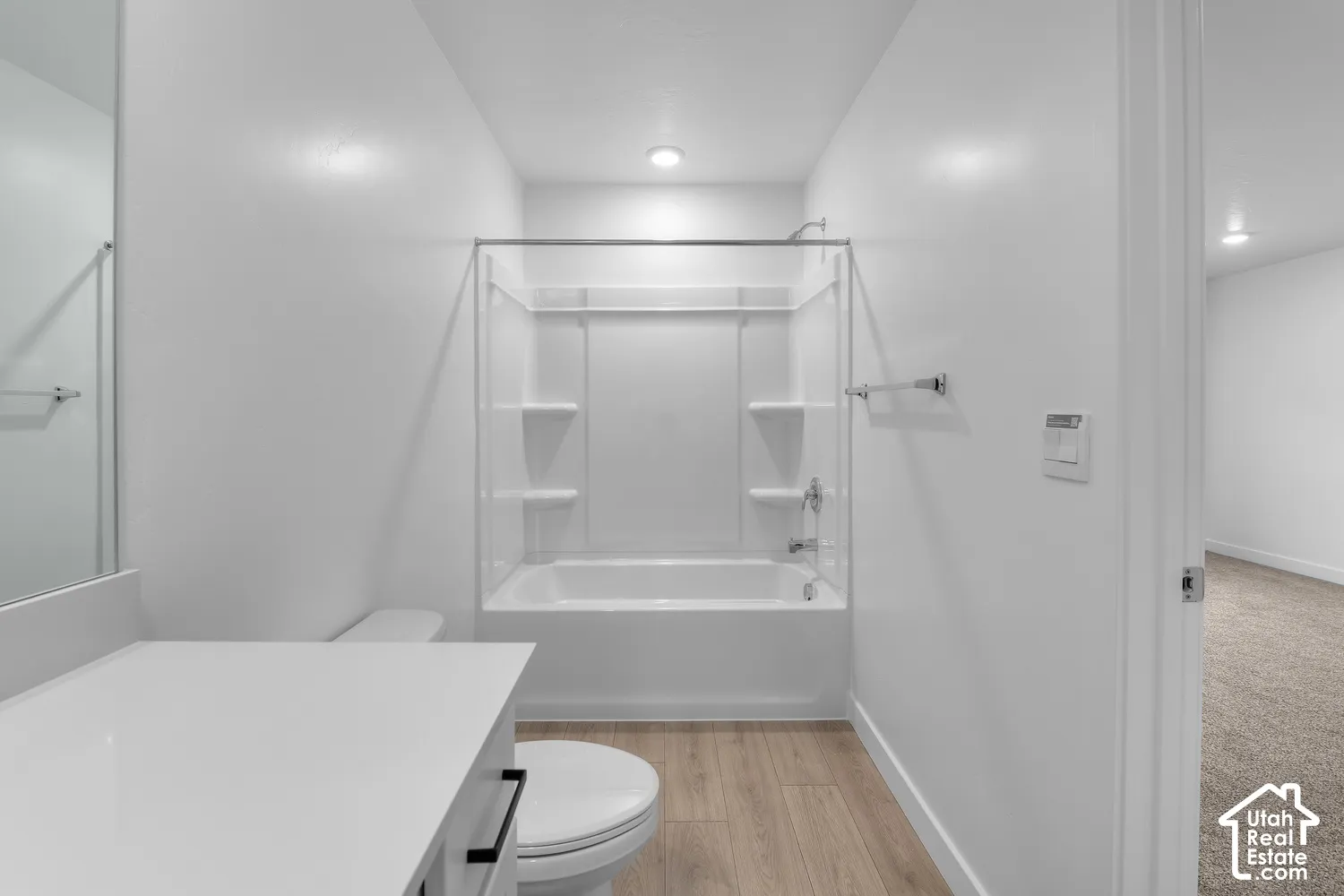 White vanity with a solid surface countertop, wood-finish flooring, and a tub/shower combination with integrated shelving