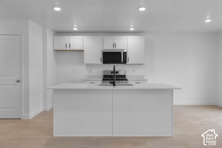 Kitchen featuring white cabinetry, a central island with an integrated sink, stainless steel appliances, recessed lighting, and wood-finish flooring