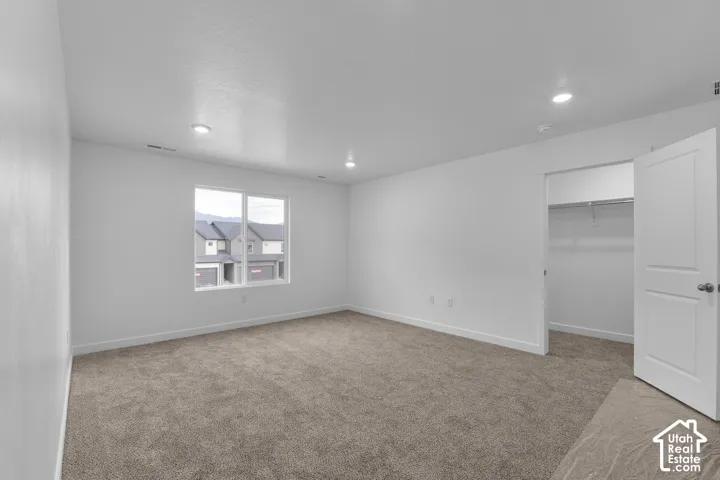 Broadloom carpeting, recessed ceiling lighting, a window with exterior visibility, and an open closet with a hanging rod