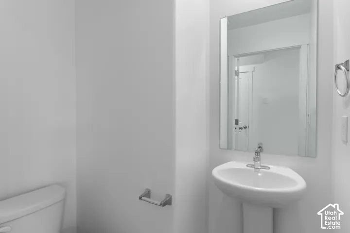 Pedestal sink with chrome faucet, wall-mounted rectangular mirror, and white toilet