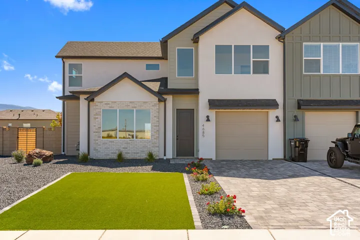 Modern exterior featuring varied siding, an attached garage, a paver driveway, and an artificial turf lawn