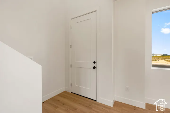 White interior door with dark hardware, light wood-finish flooring, white walls, and a window providing natural light