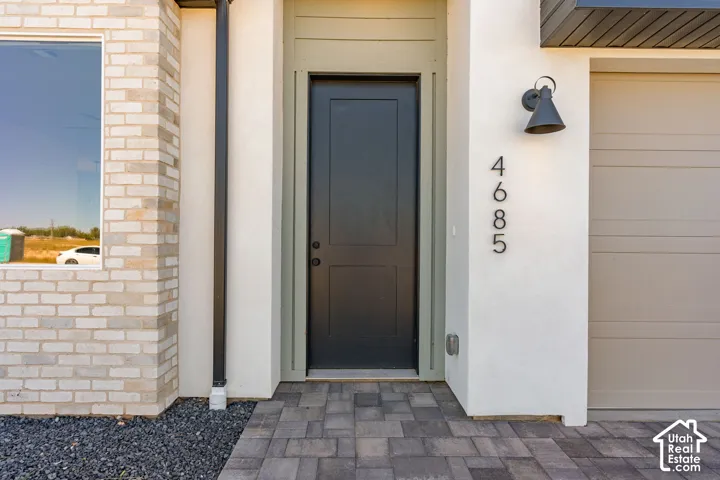White brick exterior with a dark entry door, modern sconce lighting, and a paved walkway