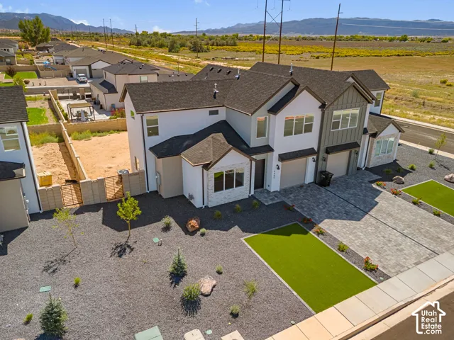 Contemporary exterior featuring white and gray siding, stone accents, multiple garage doors, a paved driveway, and low-maintenance landscaping with artificial turf sections