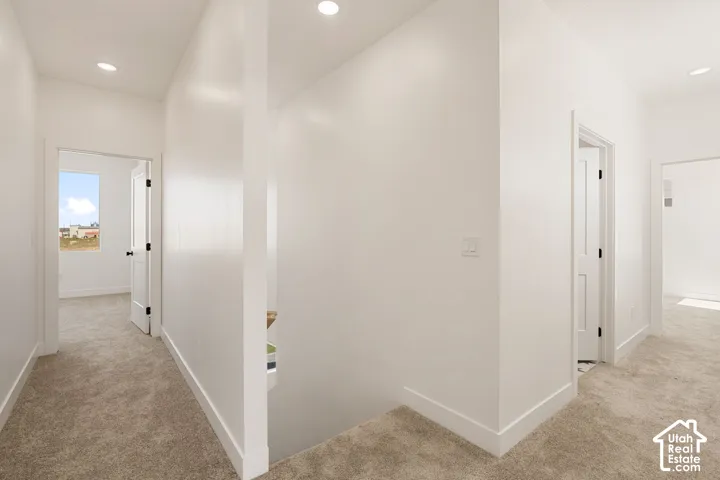 Recessed ceiling lights illuminate a hallway with light-colored carpeting, white walls, and white trim