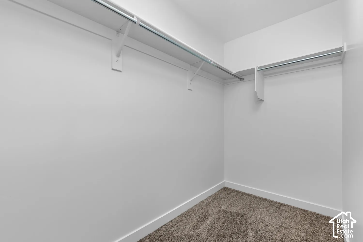 White painted walls with white trim and gray carpeting, featuring dual metal hanging rods and shelving