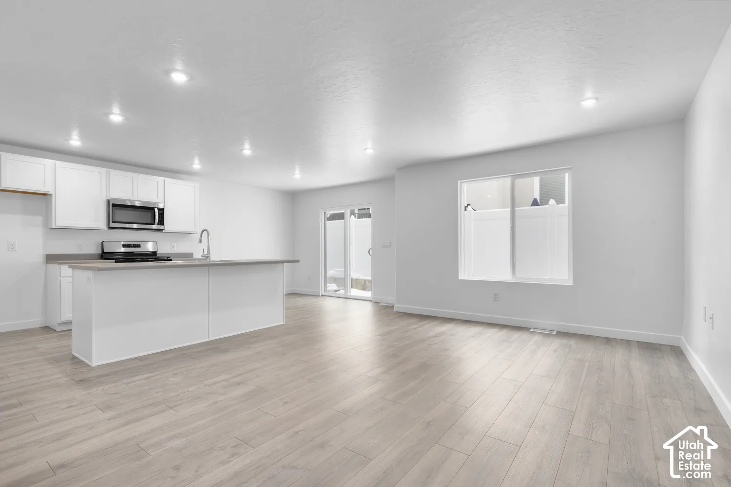 White cabinetry kitchen with stainless steel appliances, central island with sink, wood-finish flooring, and recessed lighting