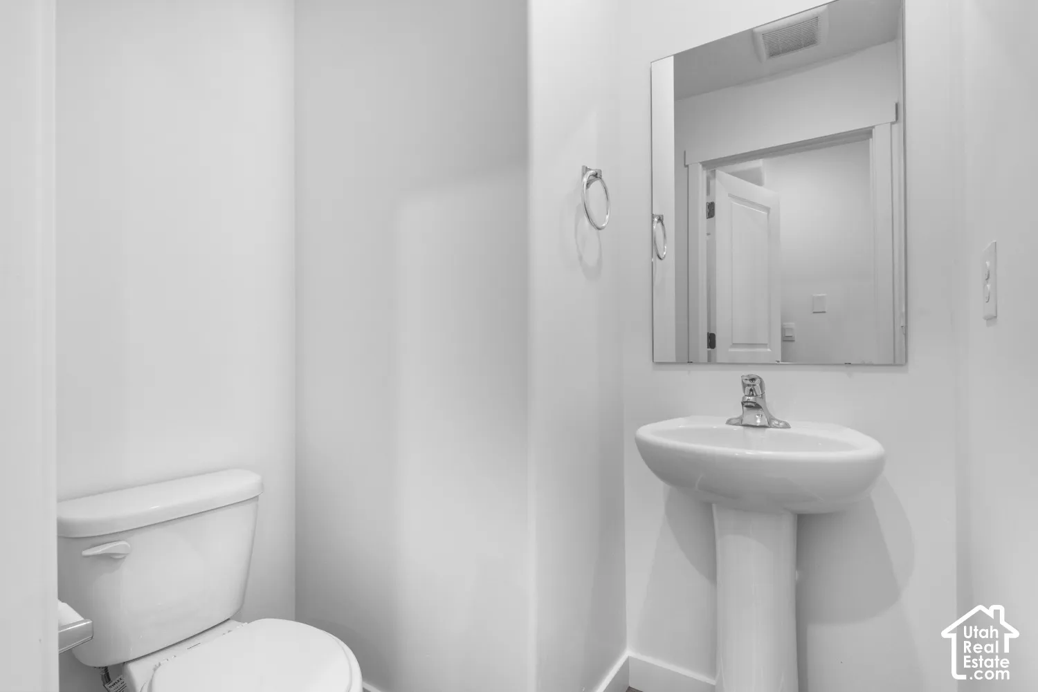 Pedestal sink with a chrome faucet, wall-mounted mirror, and a white toilet