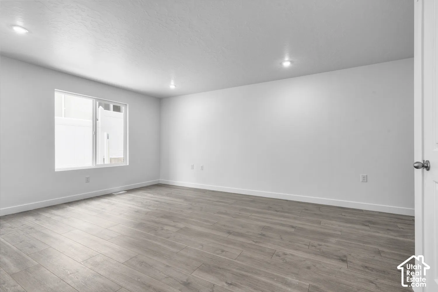 Recessed ceiling lighting, white painted walls, wood-finish flooring, and a white framed window