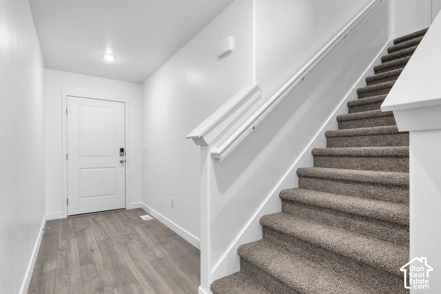 Entryway featuring wood-finish flooring, a white paneled door with smart lock hardware, and a carpeted staircase with a white railing