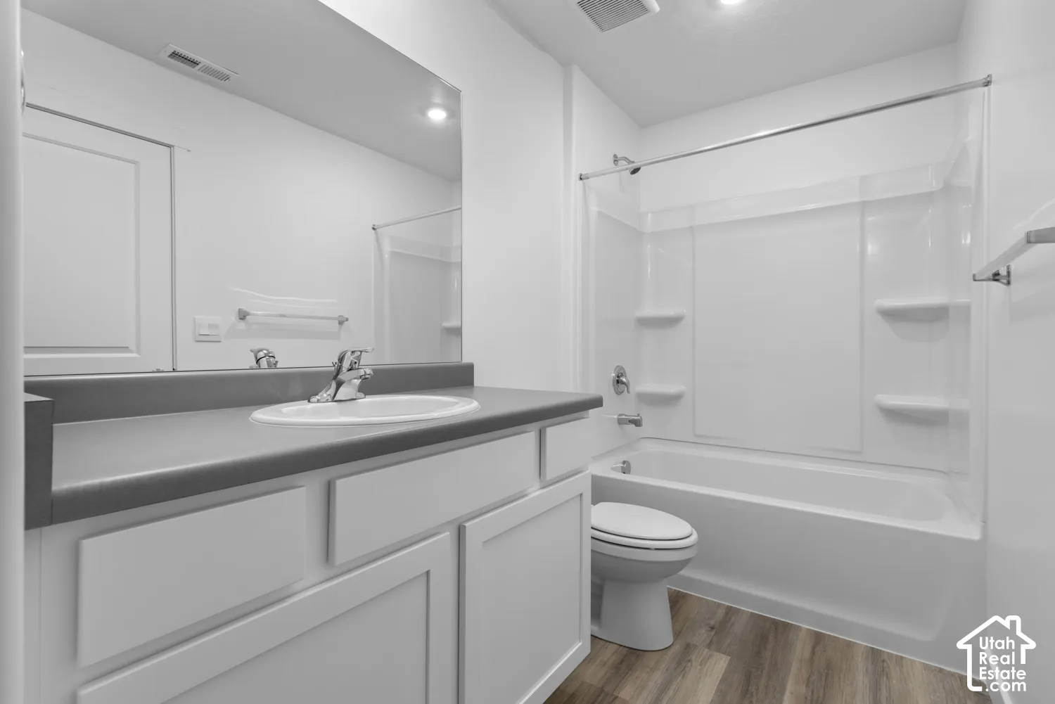 Bathroom featuring a single vanity with an integrated sink, a rectangular mirror, wood-finish flooring, and a white tub with an integrated shower