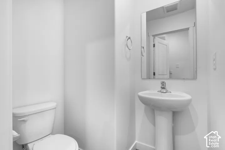 Pedestal sink with a chrome faucet, wall-mounted mirror, and a white toilet