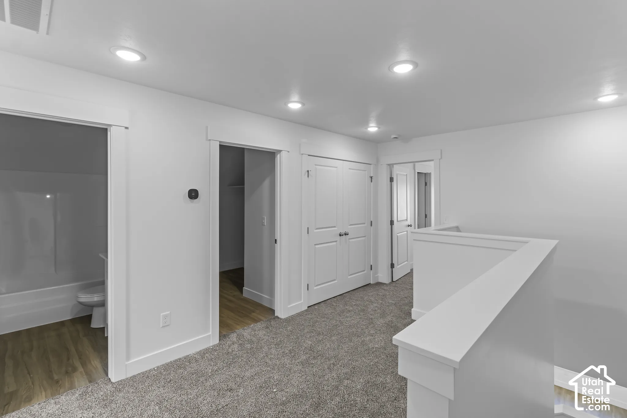 Recessed lighting illuminates the upper hall, featuring carpeted flooring and white painted walls