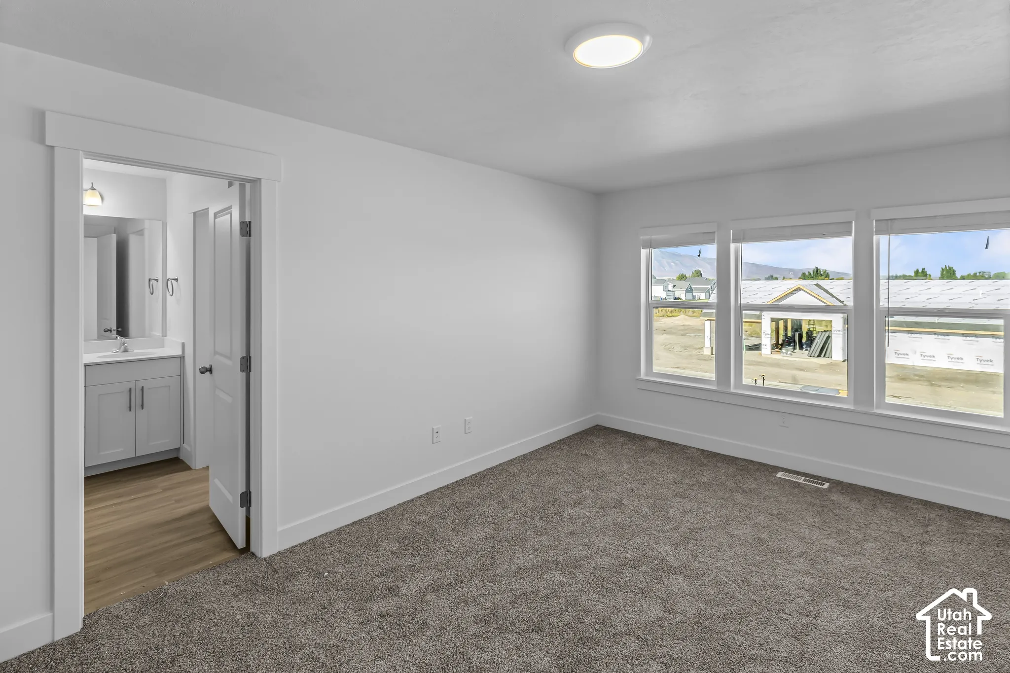 Plush carpet flooring, three large windows, recessed lighting, and a neutral color palette