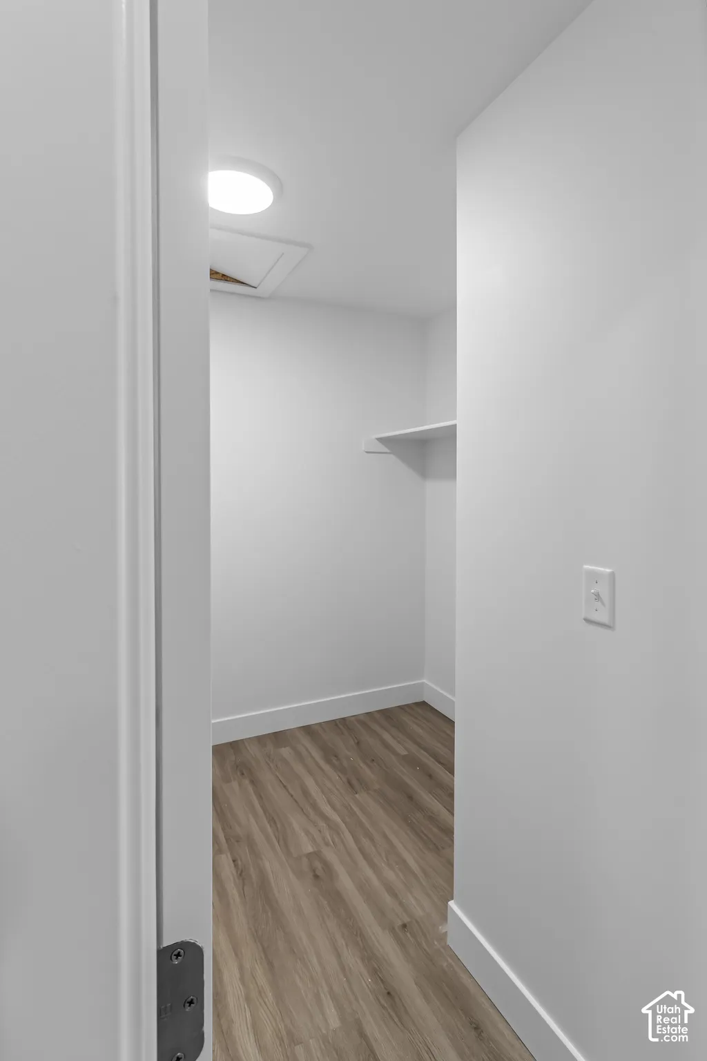 Wood-finish flooring with white baseboards, a single wall shelf, and a ceiling-mounted light fixture