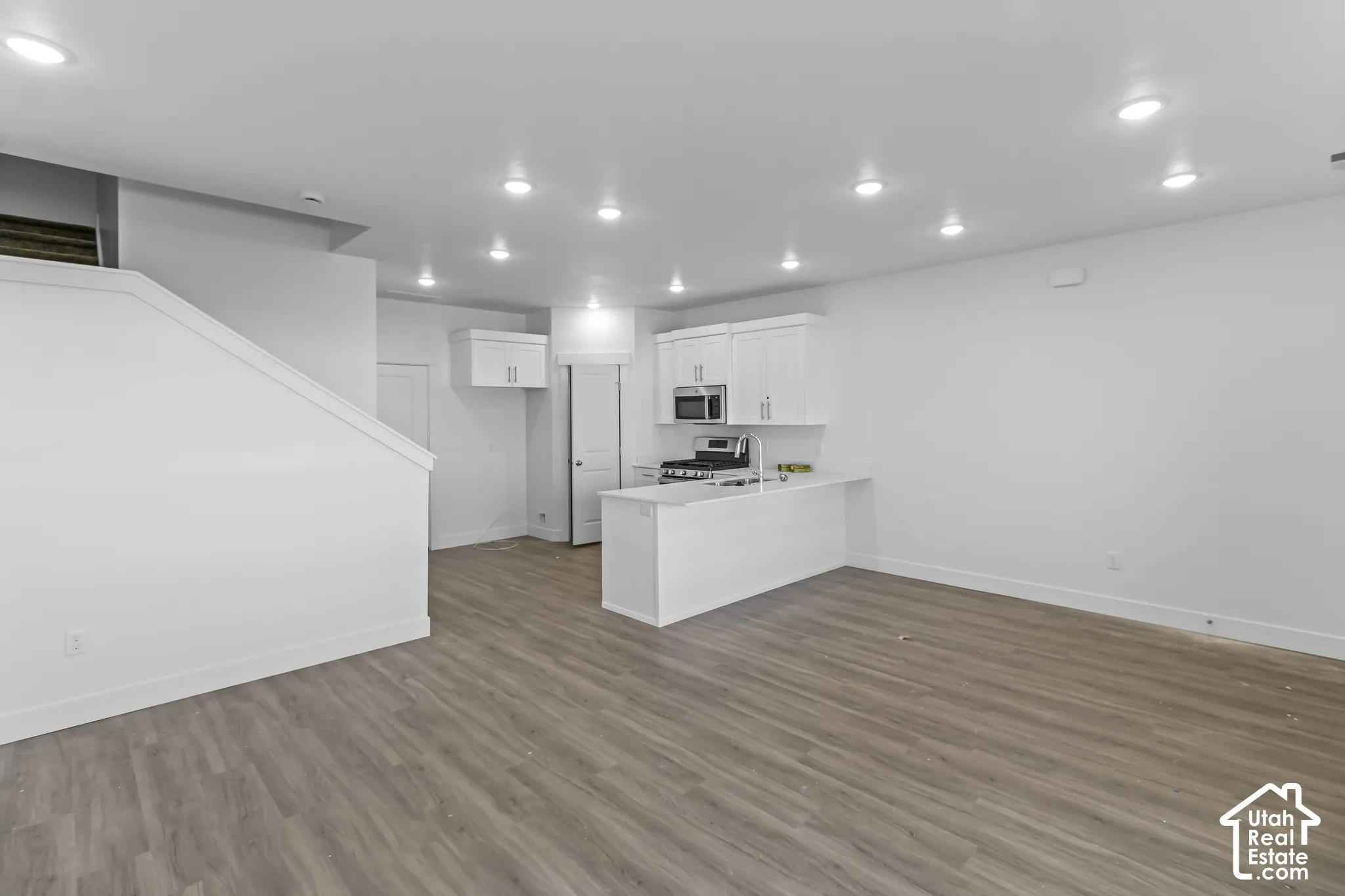 Open concept living area with wood-finish flooring, recessed lighting, and a kitchen featuring white cabinetry, stainless steel appliances, and a peninsula with a bar counter