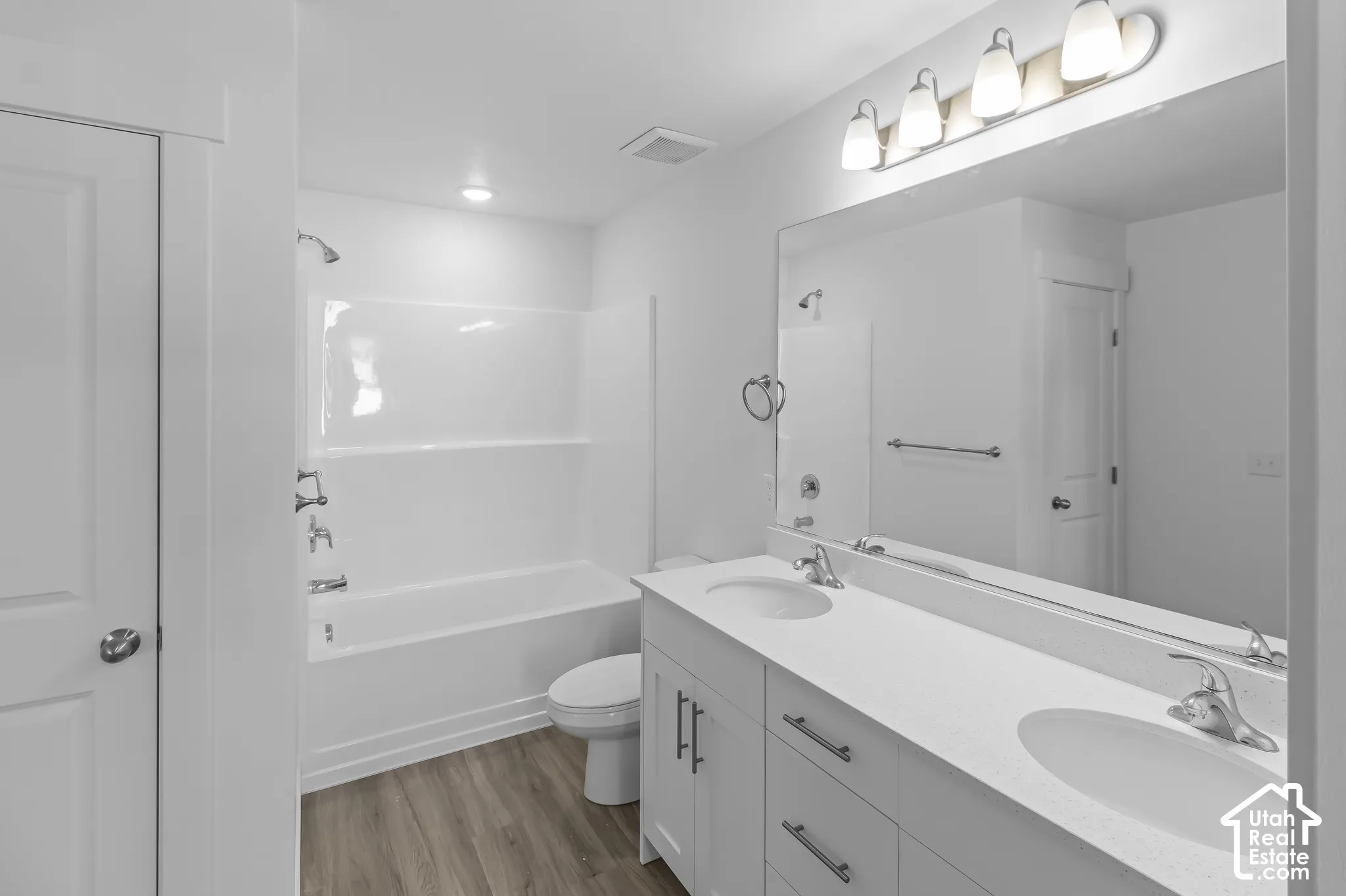 Dual vanity with integrated sinks, brushed nickel fixtures, white cabinetry, a large wall-mounted mirror, and wood-finish flooring