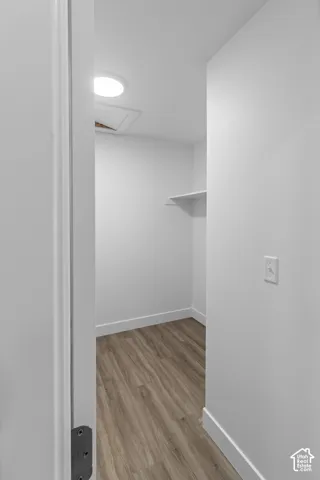 Wood-finish flooring with white baseboards, a single wall shelf, and a ceiling-mounted light fixture