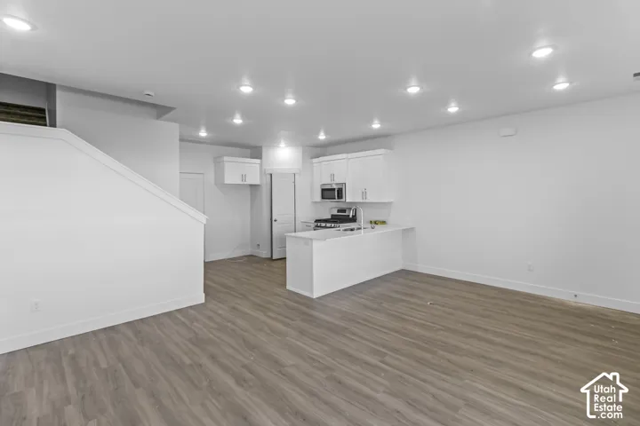 Open concept living area with wood-finish flooring, recessed lighting, and a kitchen featuring white cabinetry, stainless steel appliances, and a peninsula with a bar counter