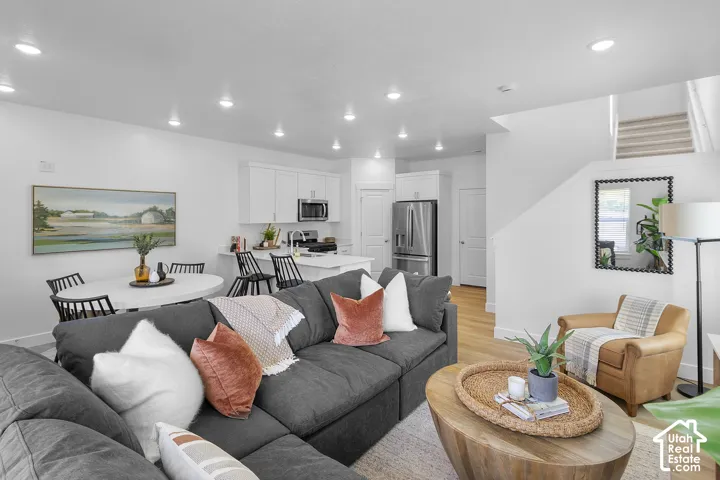 Open-concept living space featuring wood-finish flooring, recessed lighting, and a white kitchen with stainless steel appliances