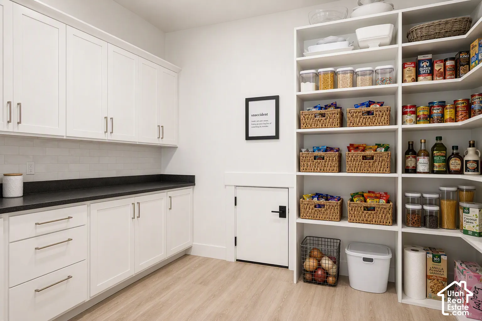 White cabinetry with brushed nickel hardware, dark countertops, a white subway tile backsplash, light wood-finish flooring, and built-in shelving