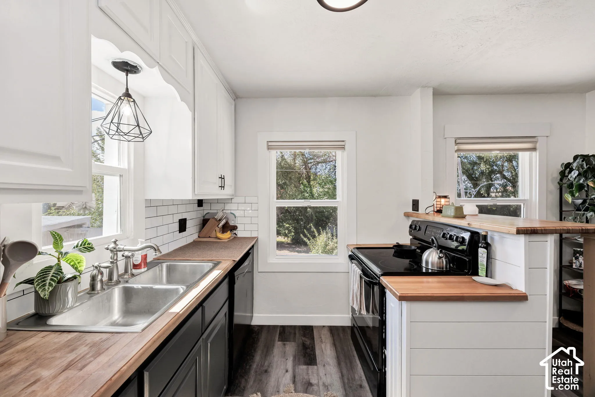 Kitchen featuring wood-finish countertops, white shaker-style upper cabinetry, black lower cabinetry, stainless steel double basin sink, and a subway tile backsplash