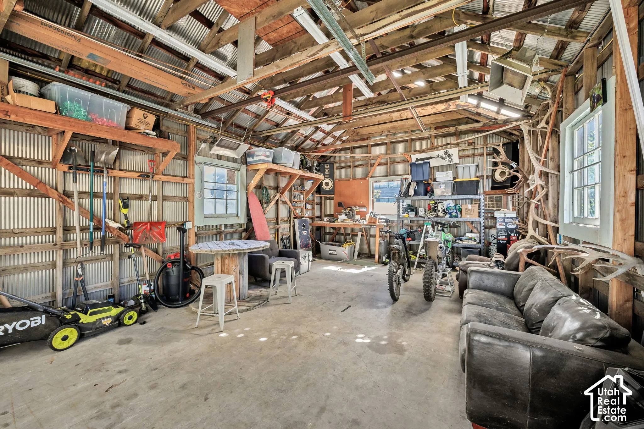 Large open garage with concrete flooring, exposed wood beam ceiling, and multiple windows