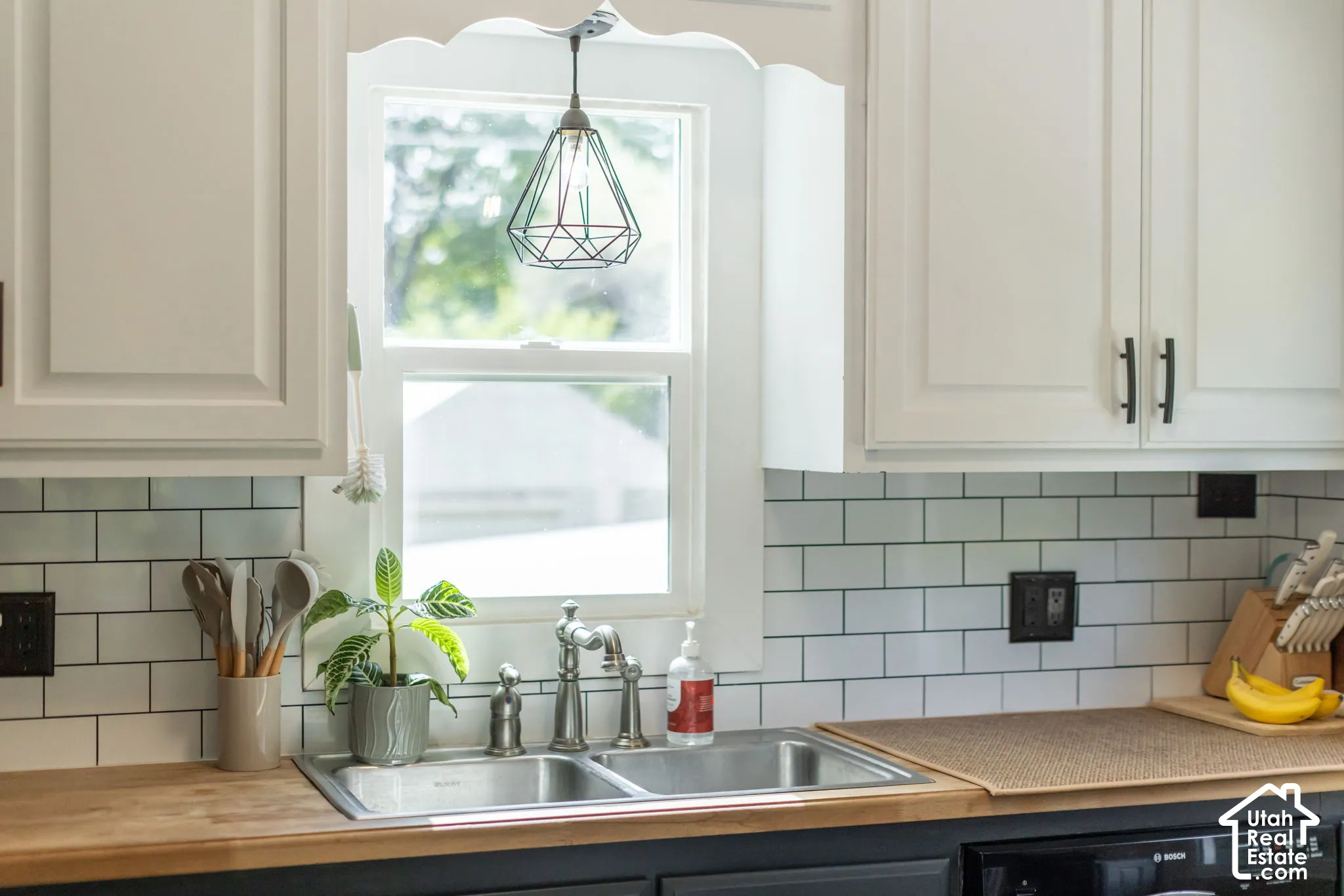 White shaker-style cabinetry with matte black hardware, subway tile backsplash, wood-finish countertops, and a double basin stainless steel sink