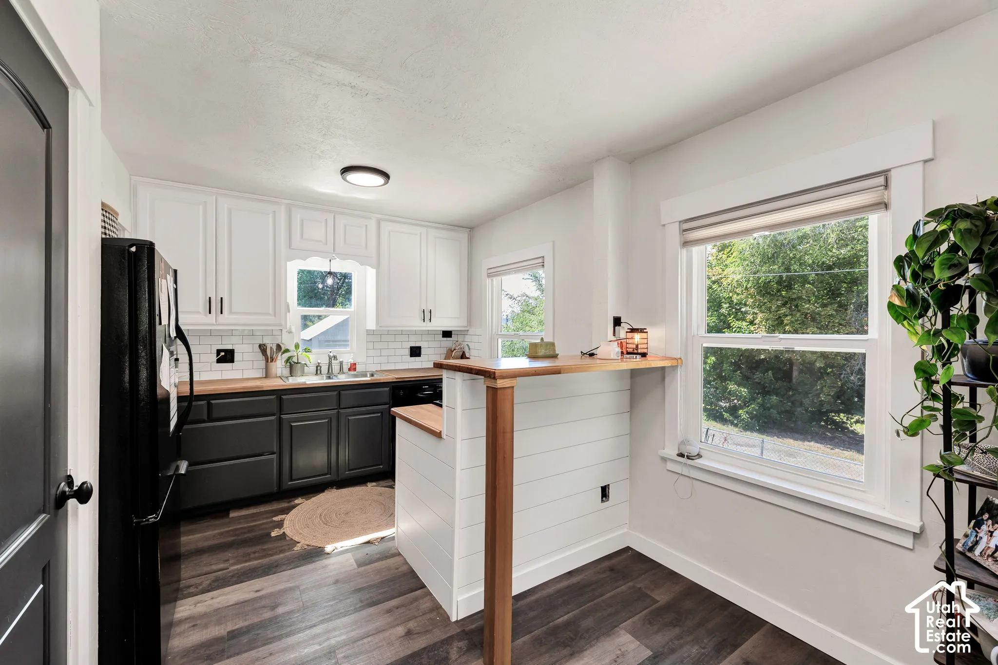 Wood-finish LVP flooring, white upper cabinetry, lower cabinetry in a dark finish, wood countertops, and a white subway tile backsplash