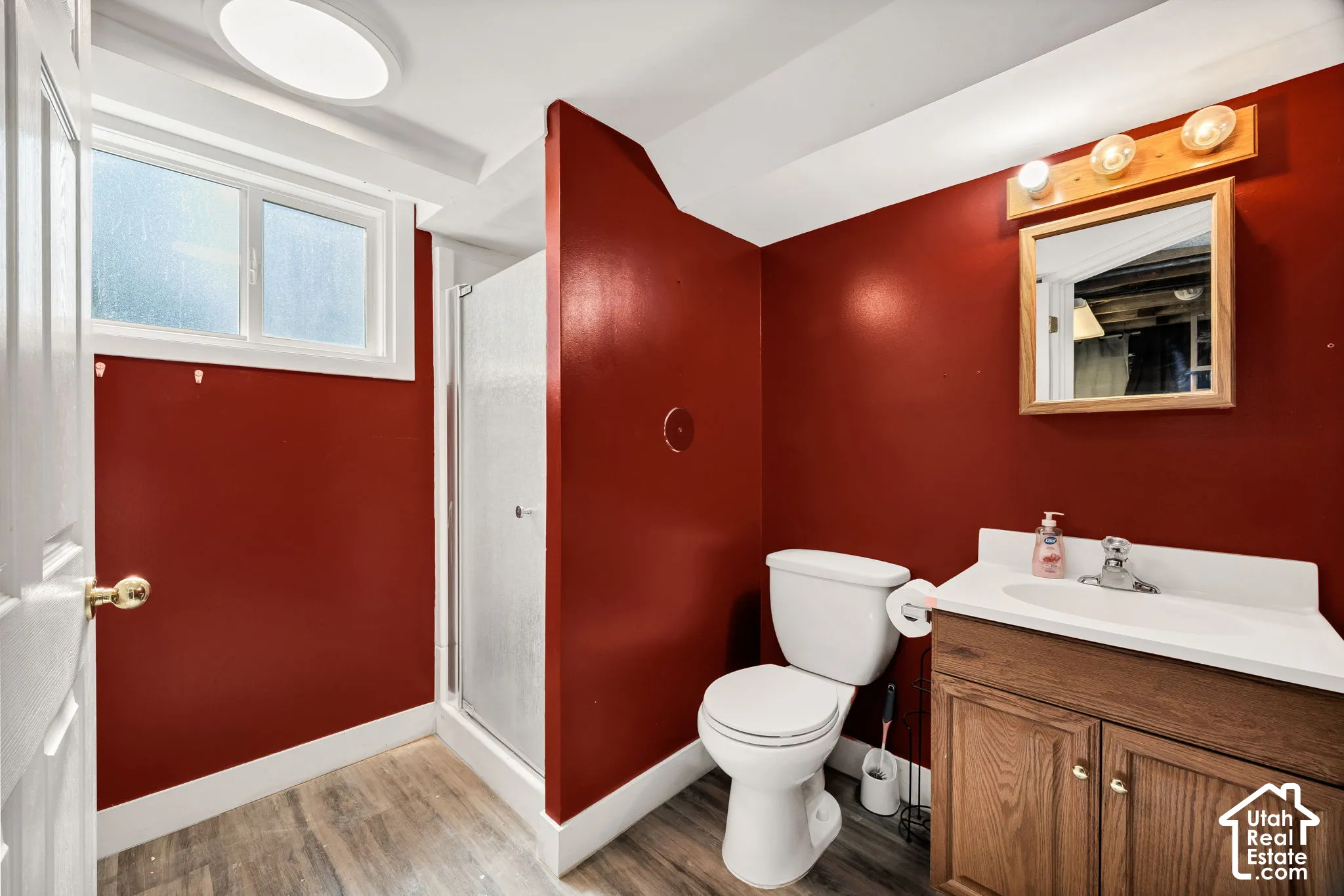 Wood-finish flooring, white window trim, and a built-in shower stall