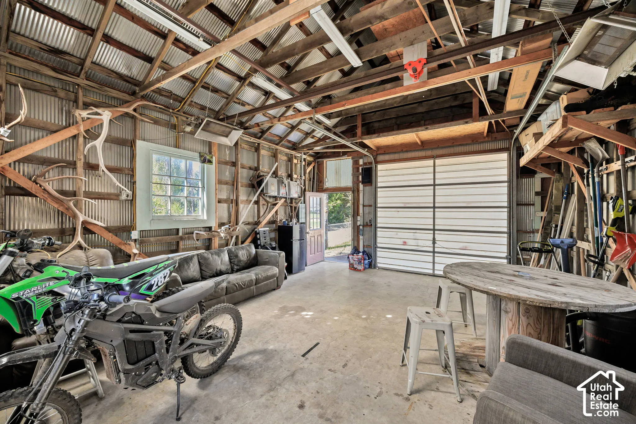 Corrugated metal walls, exposed wood beam ceiling, concrete flooring, and a large roll-up door