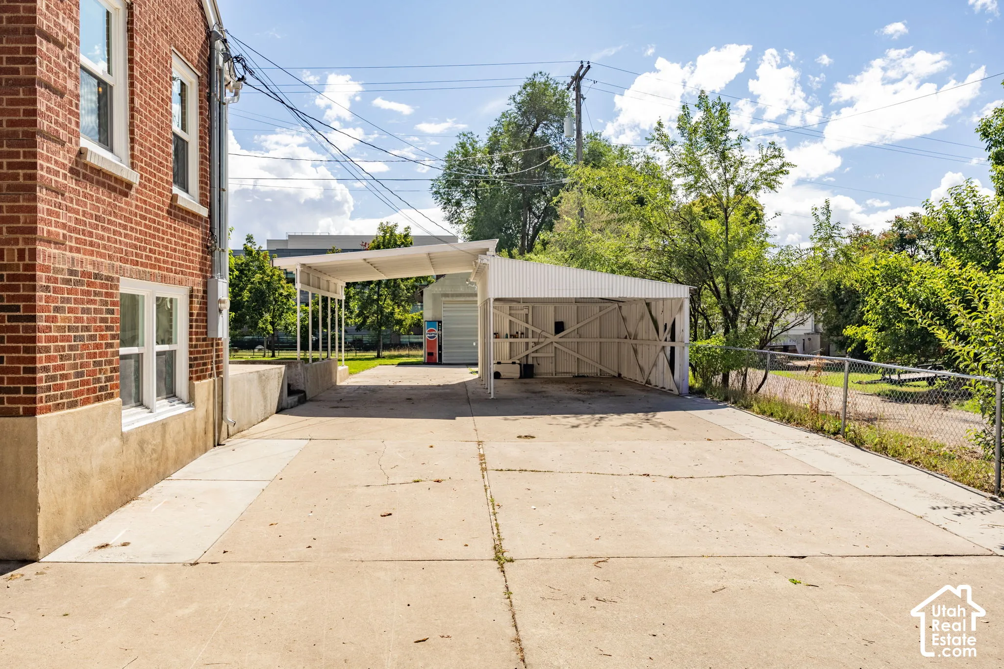 Expansive concrete driveway leading to a covered carport and a detached garage, featuring a brick exterior with white-framed windows